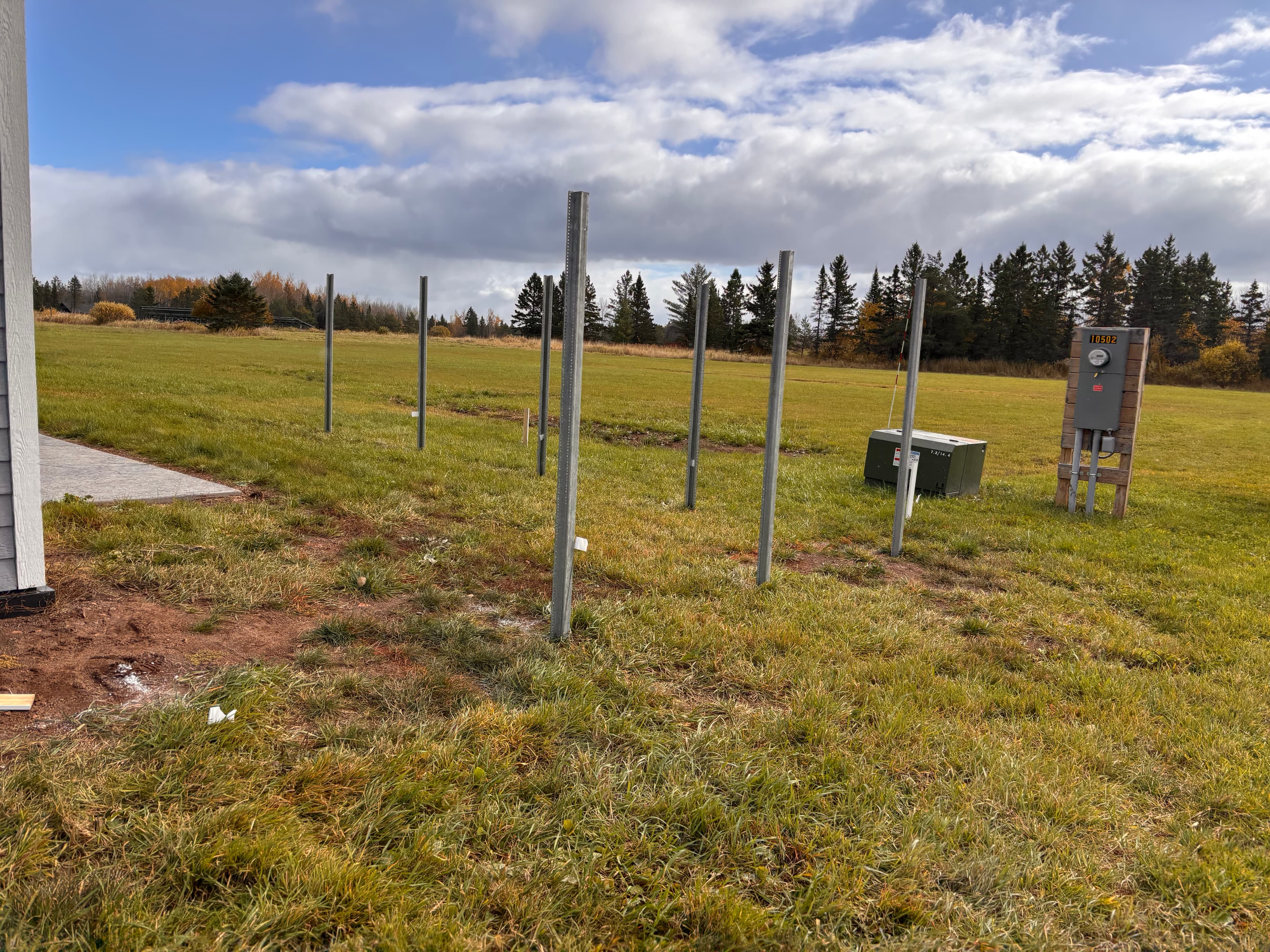 Metal posts in a grassy field with an electrical meter and a distant treeline.