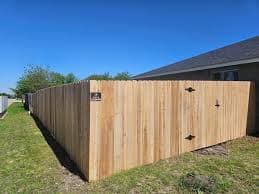New light brown wooden privacy fence with a gate bordering a residential backyard.