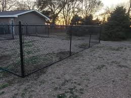 Black chain-link fence surrounding a residential backyard with a house and trees at sunset.